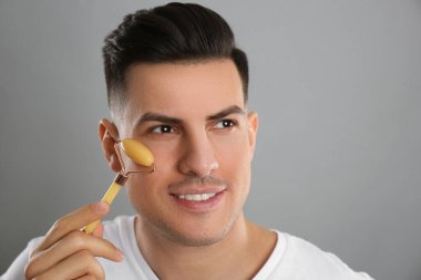Adam gri arka planda mineral yüz silindiri kullanıyor. Metin için boşluk