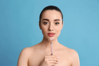 Açık mavi arka planda doğal pembe kuvars yüz silindiri kullanan kadın