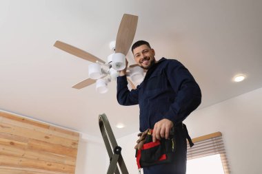 Elektrikçi tavan vantilatörünü içeride lambayla onarıyor.