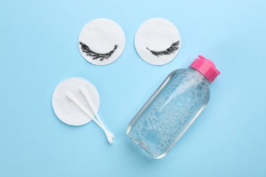 Dirty cotton pads, swabs and micellar cleansing water on light blue background, flat lay clipart