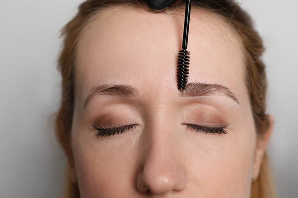 美容師ブラッシング女性の眉毛の前に光グレーの背景に着色 クローズアップ — ストック写真