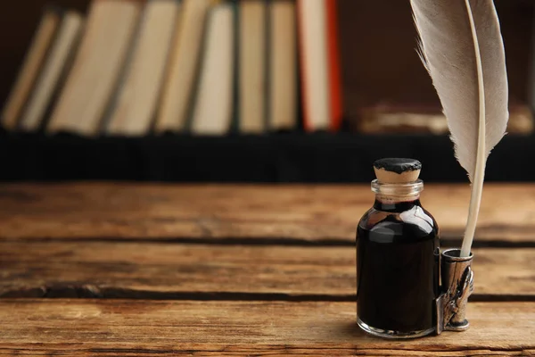 Feather pen and bottle of ink on wooden table. Space for text