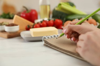 Masadaki ürünlerin yanında deftere yazan kadın, yakın çekim. Keto diyeti