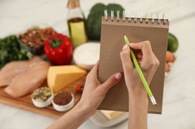 Masadaki ürünlerin yanında deftere yazan kadın, yakın çekim. Keto diyeti