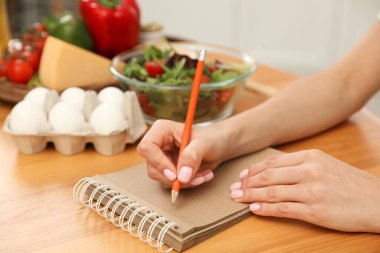 Masadaki ürünlerin yanında deftere yazan kadın, yakın çekim. Keto diyeti