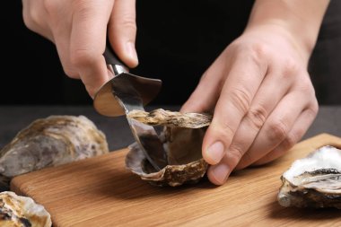 Gri masada taze istiridyeyi bıçakla açan adam, yakın plan.