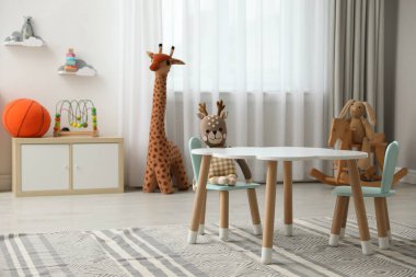 Çocuk odasının içinde şık masa, sandalye ve oyuncaklar var.