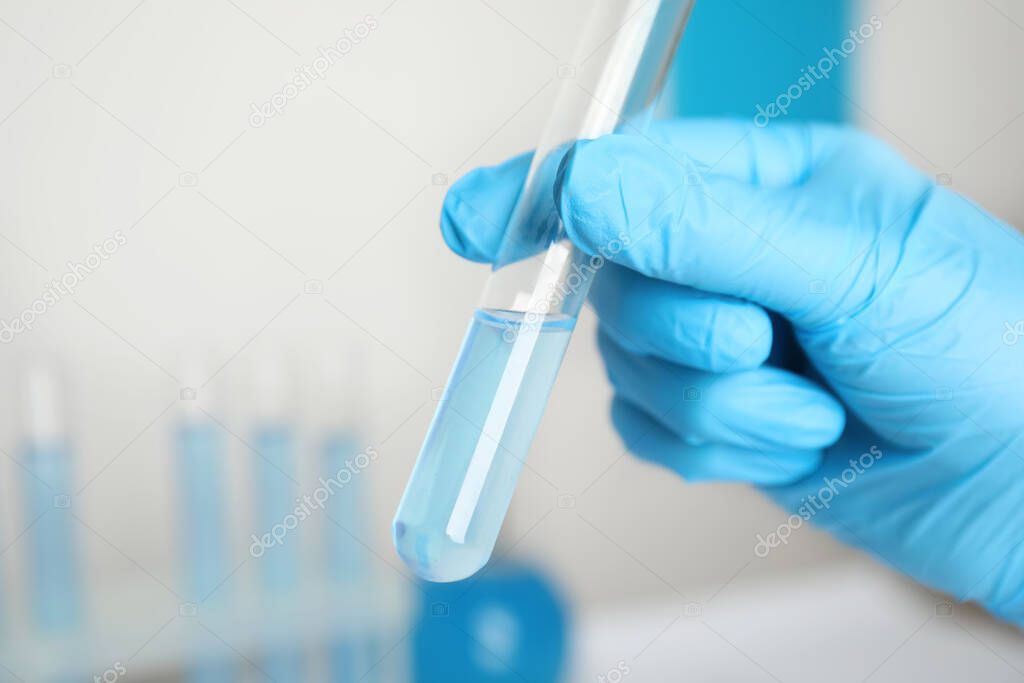 Scientist holding test tube with liquid in laboratory, closeup