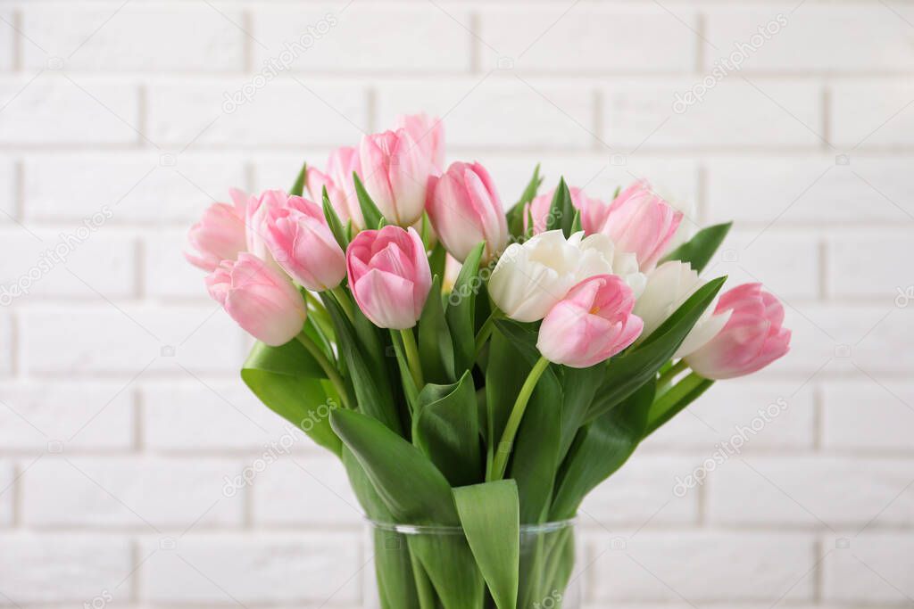 Beautiful bouquet of tulips in glass vase against white brick wall