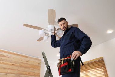 Elektrikçi tavan vantilatörünü içeride lambayla onarıyor.