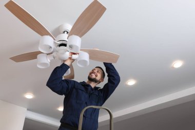 Elektrikçi tavan vantilatörünü içeride lambayla onarıyor.