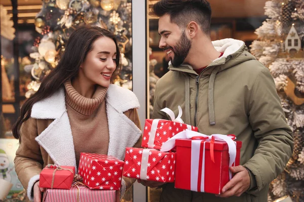 クリスマスのために屋外で装飾された店の近くのプレゼントと素敵なカップル — ストック写真