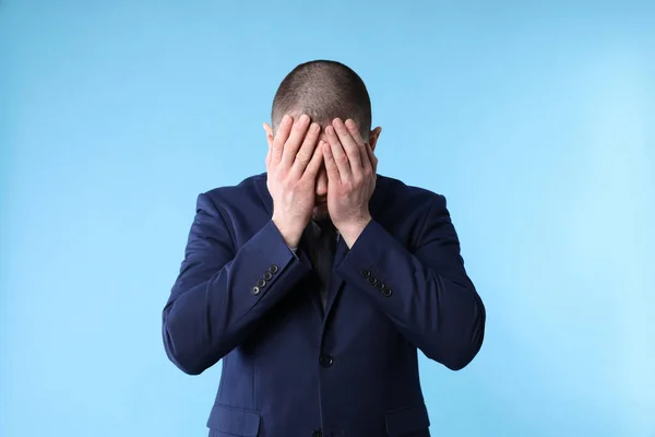 stock image Upset man in suit closing his face with hands on light blue background