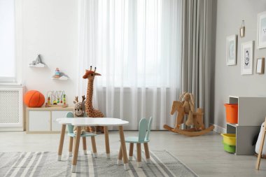 Çocuk odasının içinde şık masa, sandalye ve oyuncaklar var.