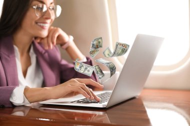 İnternetten para kazanıyorum. Masada dizüstü bilgisayar kullanan ve dolar uçuran bir kadın.