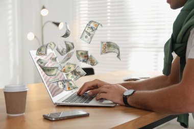 İnternetten para kazanıyorum. Masada dizüstü bilgisayar kullanan ve dolar uçuran bir adamın yakın görüntüsü.
