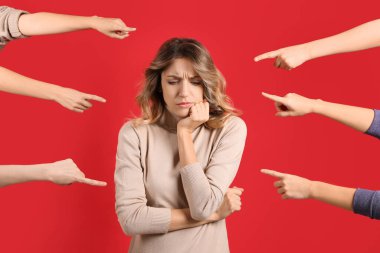 Stressed woman feeling uncomfortable because of people pointing at her against red background. Social responsibility concept clipart