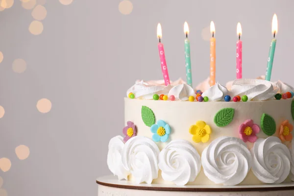 Delicious birthday cake with party decor on stand against blurred festive lights, closeup. Space for text