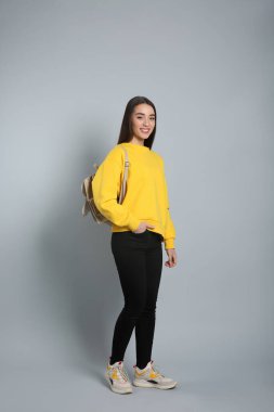 Gri arka planda zarif deri sırt çantalı güzel bir genç kadın.