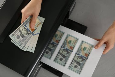 Sahtekar, gri masada dolar banknotları basıyor. Sahte para kavramı