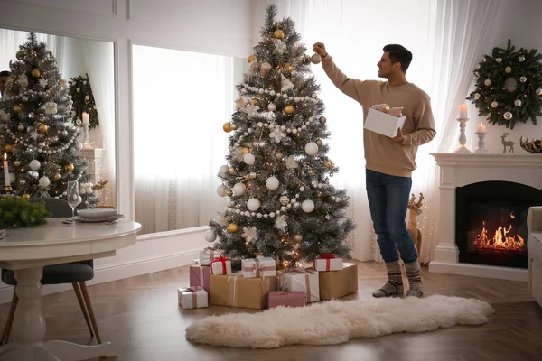 美しい部屋のインテリアでクリスマスツリーを飾る男 — ストック写真