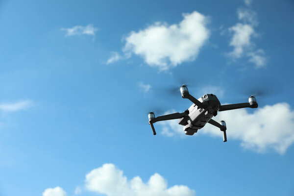 Modern drone with camera flying in sky on sunny day