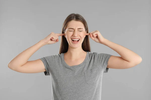 Συναισθηματική Νεαρή Γυναίκα Που Καλύπτει Αυτιά Της Δάχτυλα Γκρι Φόντο — Φωτογραφία Αρχείου