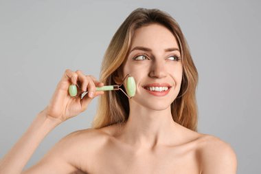 Genç bir kadın açık gri arka planda doğal yeşil yüz silindiri kullanıyor.