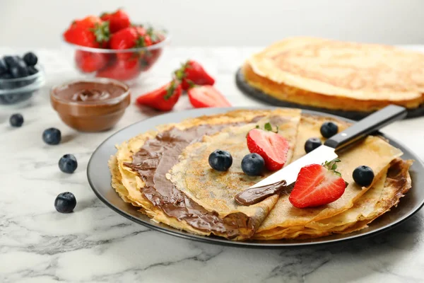 Heerlijke Dunne Pannenkoeken Met Chocoladepasta Bessen Witte Marmeren Tafel — Stockfoto