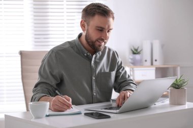 Ofisteki masada dizüstü bilgisayarda çalışan genç adam.