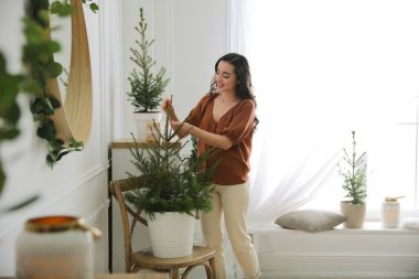 Evde Noel ışıklarıyla köknar ağacı süsleyen bir kadın.