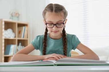 Masada kitap okuyan şirin küçük bir kız.