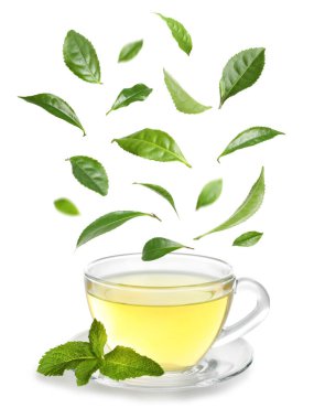 Bir fincan sıcak çay ve beyaz arka planda düşen yeşil yapraklar.