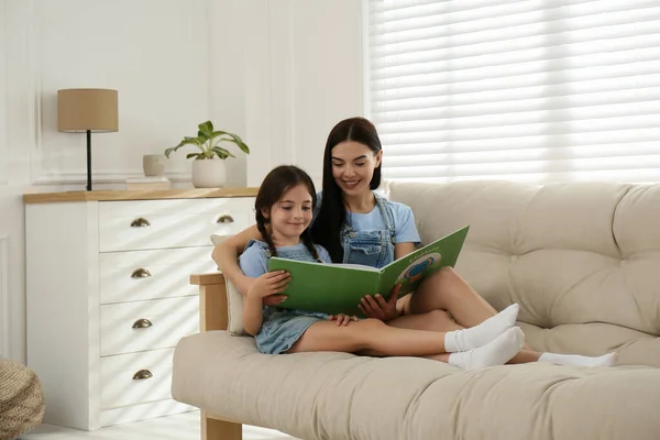 年轻的母亲和她的女儿在家里的沙发上看书 — 图库照片