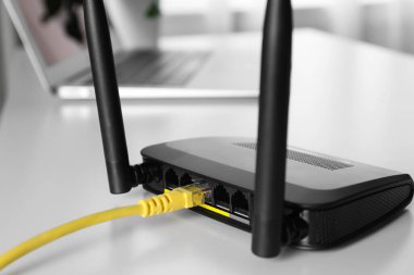 Beyaz masadaki yönlendiriciye bağlı kablo, yakın plan. Kablosuz internet iletişimi
