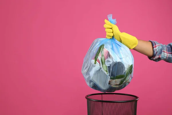 Woman taking garbage bag out of bin on pink background, closeup. Space for text