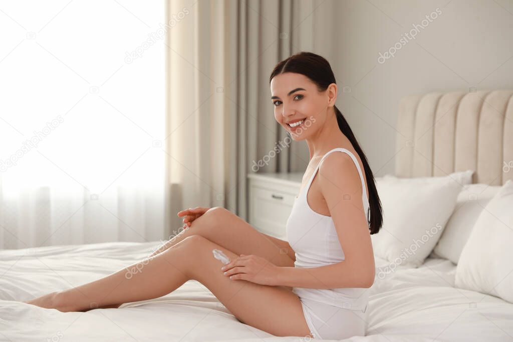 Young woman applying body cream onto her leg at home, space for text