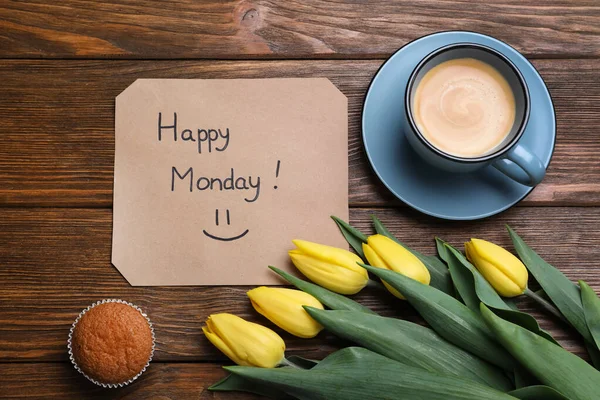 Happy Monday message, aromatic coffee, cupcake and tulips on wooden table, flat lay