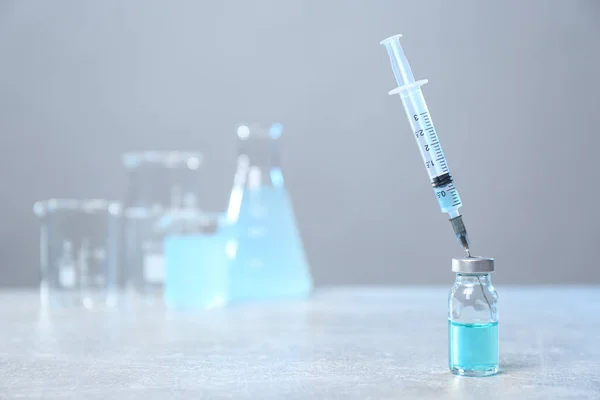 Syringe and vial on light grey table. Space for text