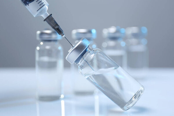 Filling syringe with medicine from vial on white table, closeup