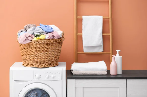 Wicker basket with dirty laundry on washing machine near coral wall indoors