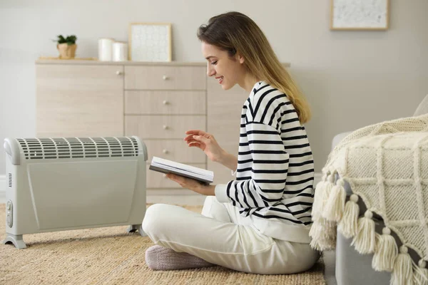 Giovane Donna Con Libro Seduta Piano Vicino Riscaldatore Elettrico Casa — Foto Stock