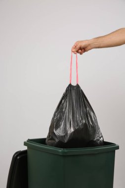 Çöp torbasını arka planda çöp kutusuna atan adam, yakın plan