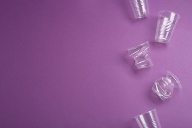 Mor arka planda plastik bardaklar, düz yatış. Metin için boşluk