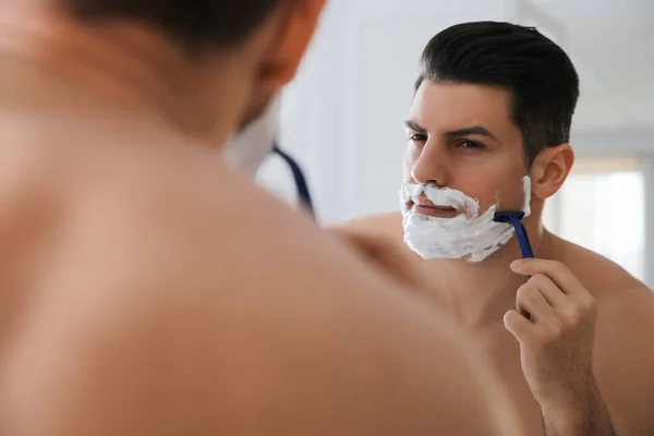 stock image Handsome man shaving near mirror in bathroom