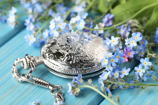 漂亮的忘记我的花和怀表放在浅蓝色的木制桌子上 — 图库照片