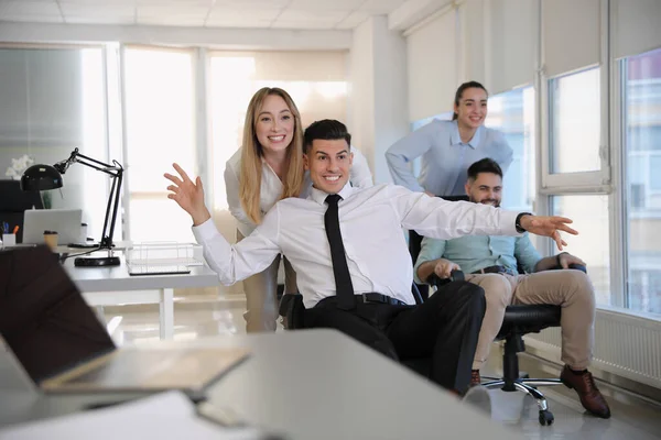 Happy office employees riding chairs at workplace