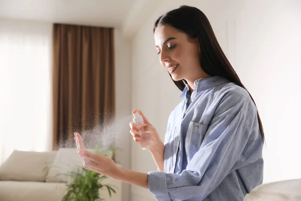 Woman applying spray sanitizer onto hand at home