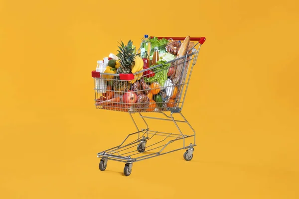 Shopping cart full of groceries on yellow background