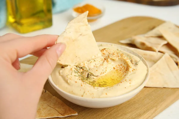 Woman dipping pita chip into hummus at table, closeup